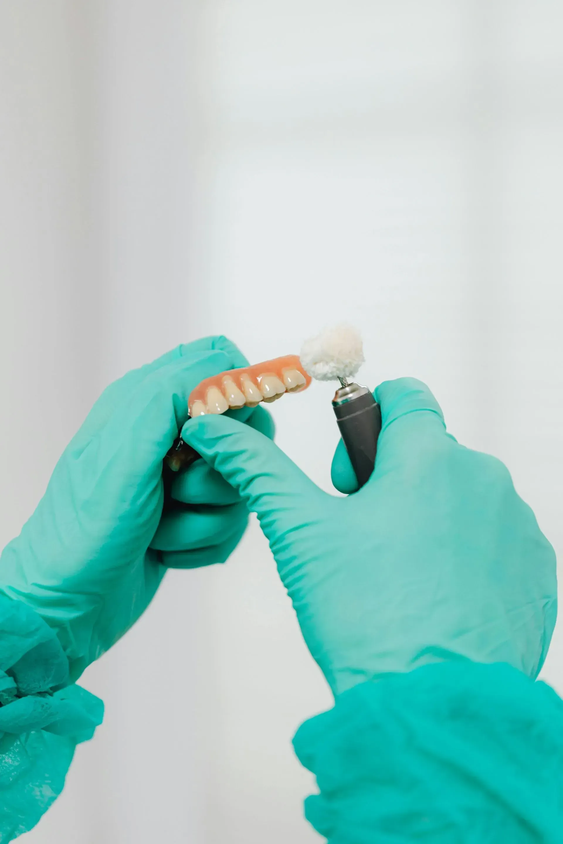 A person wearing green gloves is holding a denture in their hands.
