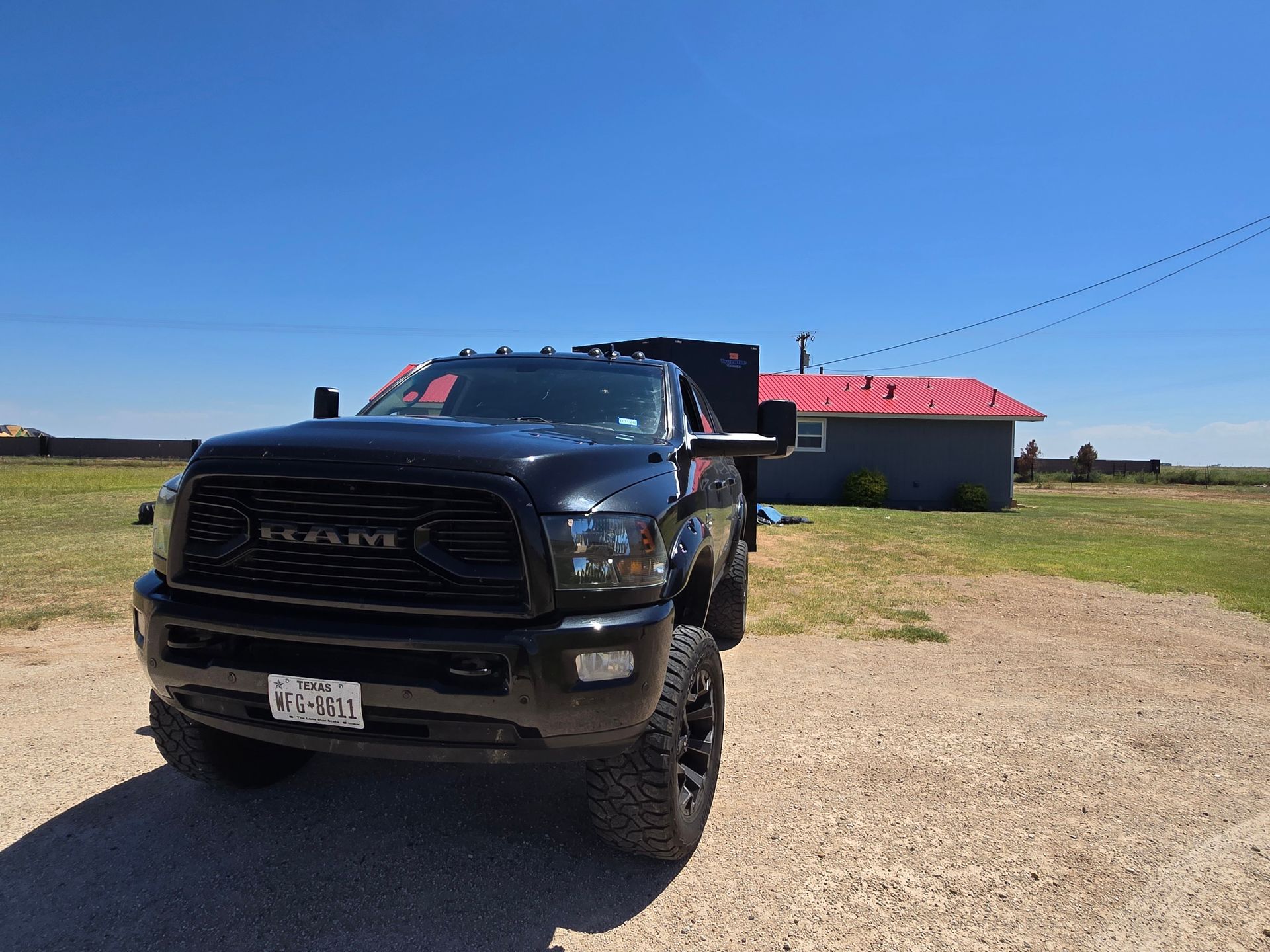 Black RAM truck parked on a gravel road beside a red-roofed building under a clear blue sky