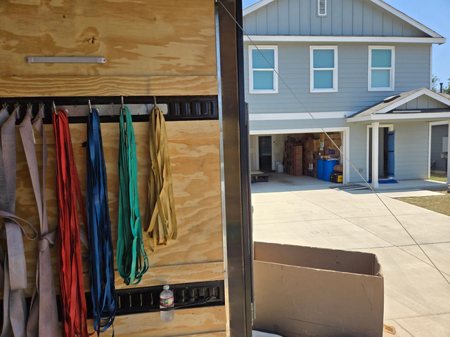 Colorful harnesses hanging on a wall beside a light blue house and driveway.