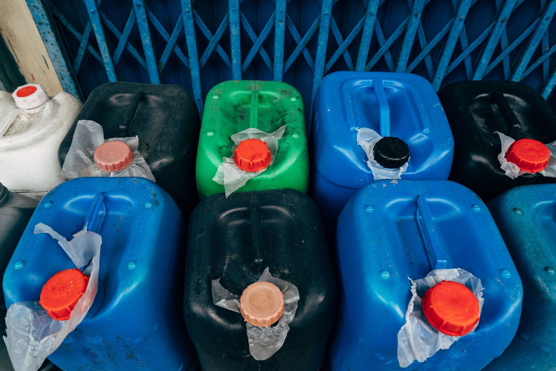 Assorted plastic jerry cans in blue, green, black, and white, lined up indoors.