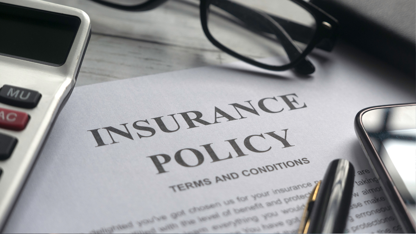 Insurance policy document on desk with calculator and glasses