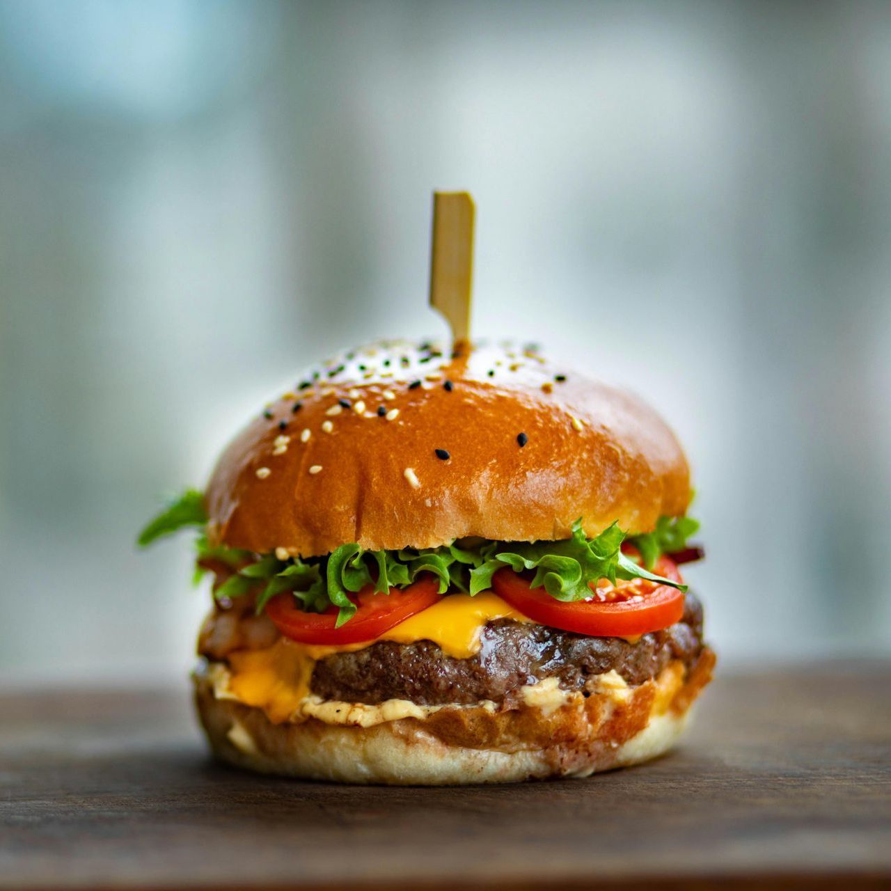 A hamburger with cheese , lettuce , tomatoes and a toothpick on a wooden table.