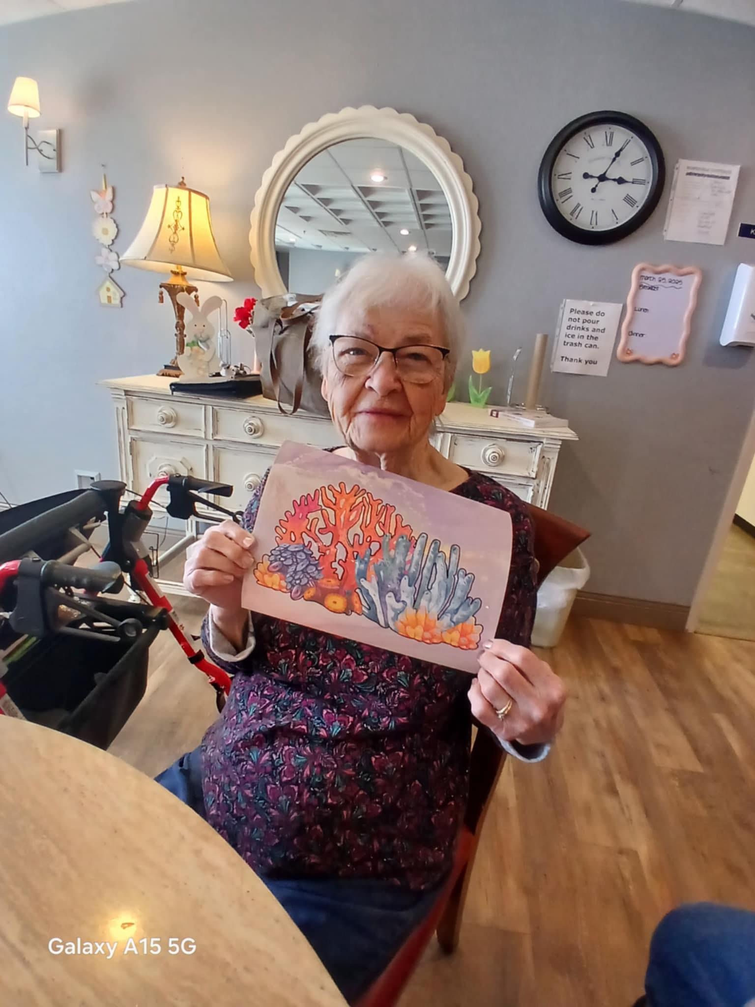 An elderly woman is sitting at a table holding a picture of a pumpkin.