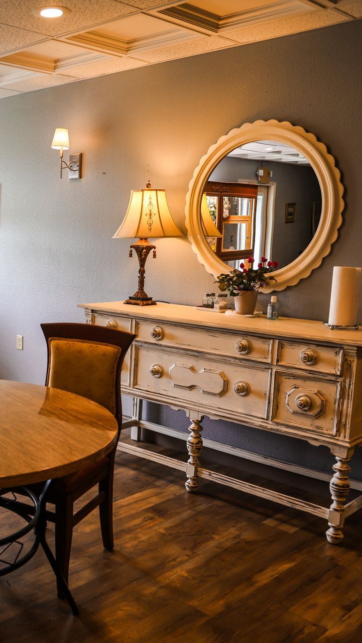 A room with a table , chairs , dresser , mirror and lamp.