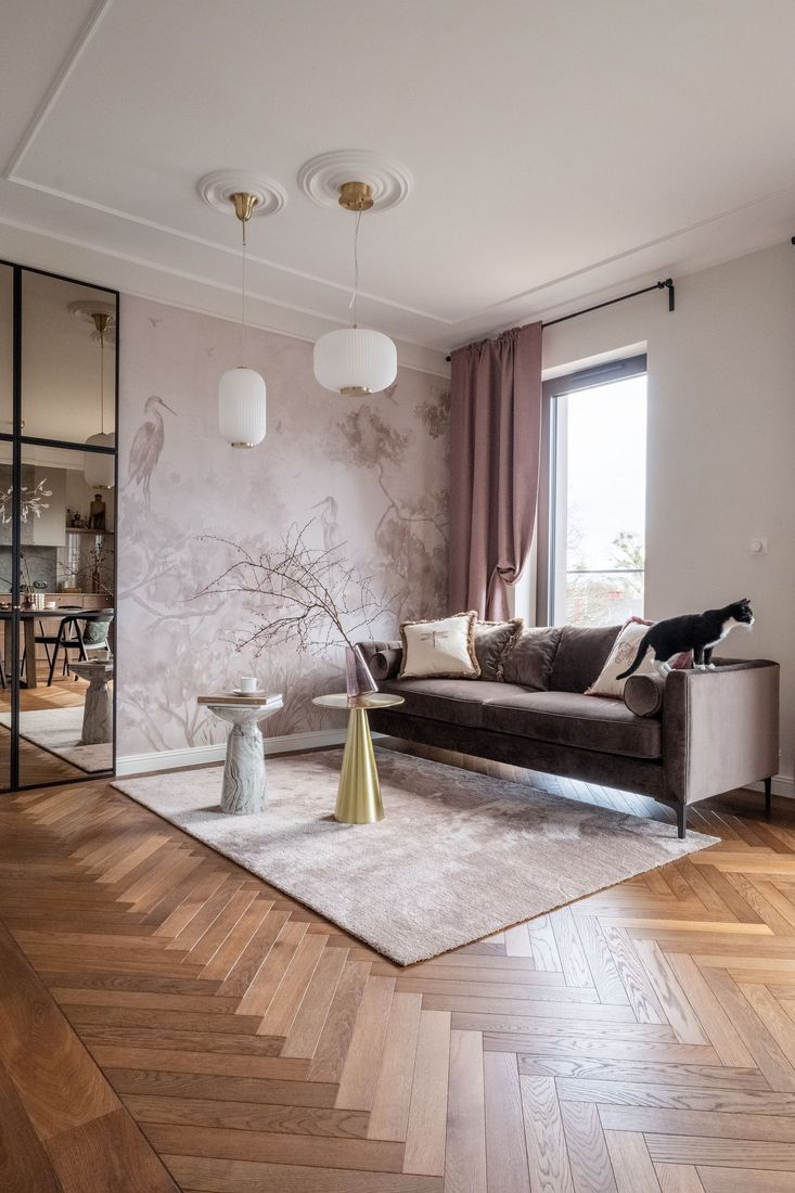 Stylish living room with pink wall, brown sofa, rug, herringbone floor, and large window with curtains