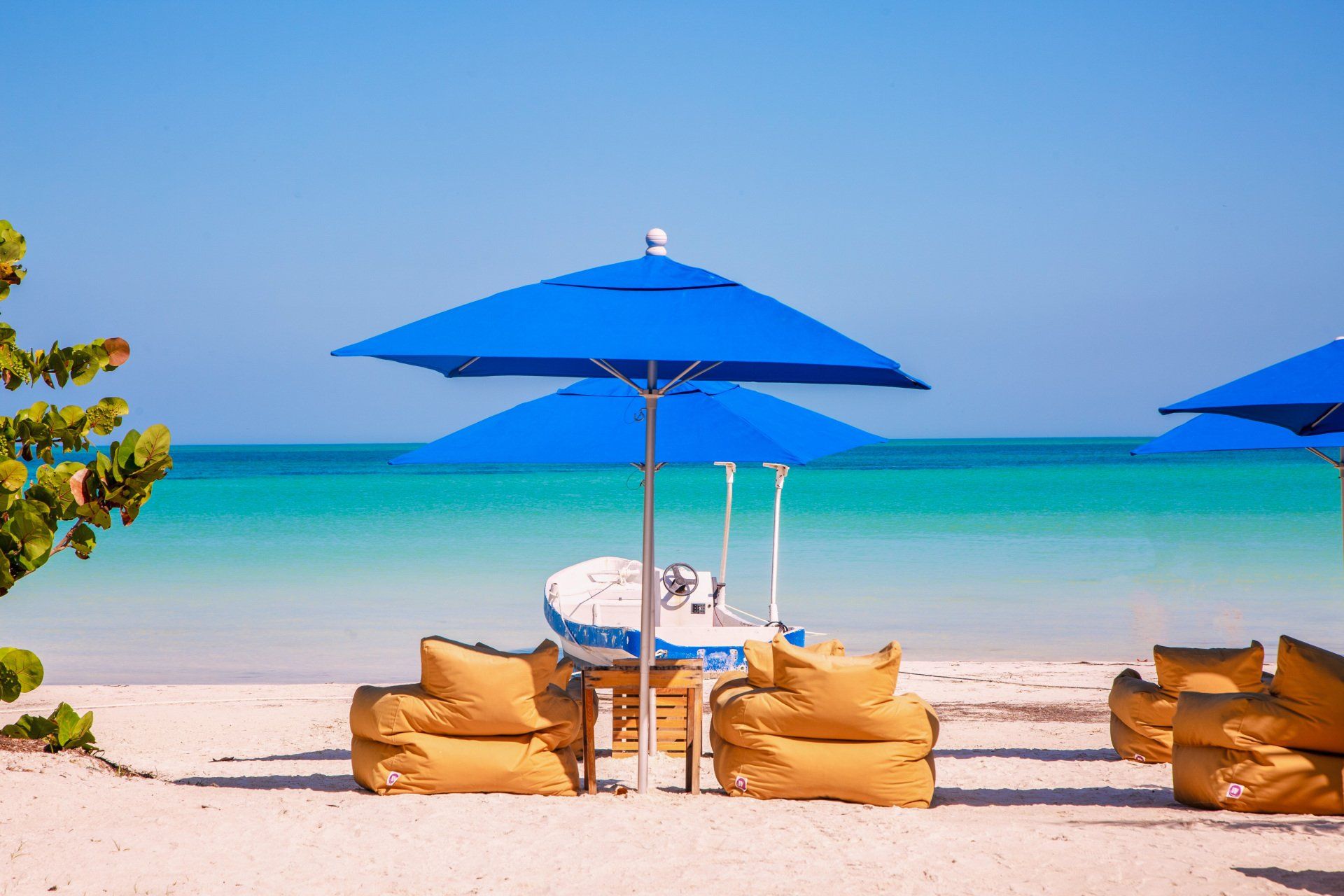 A beach with blue umbrellas and a boat in the background