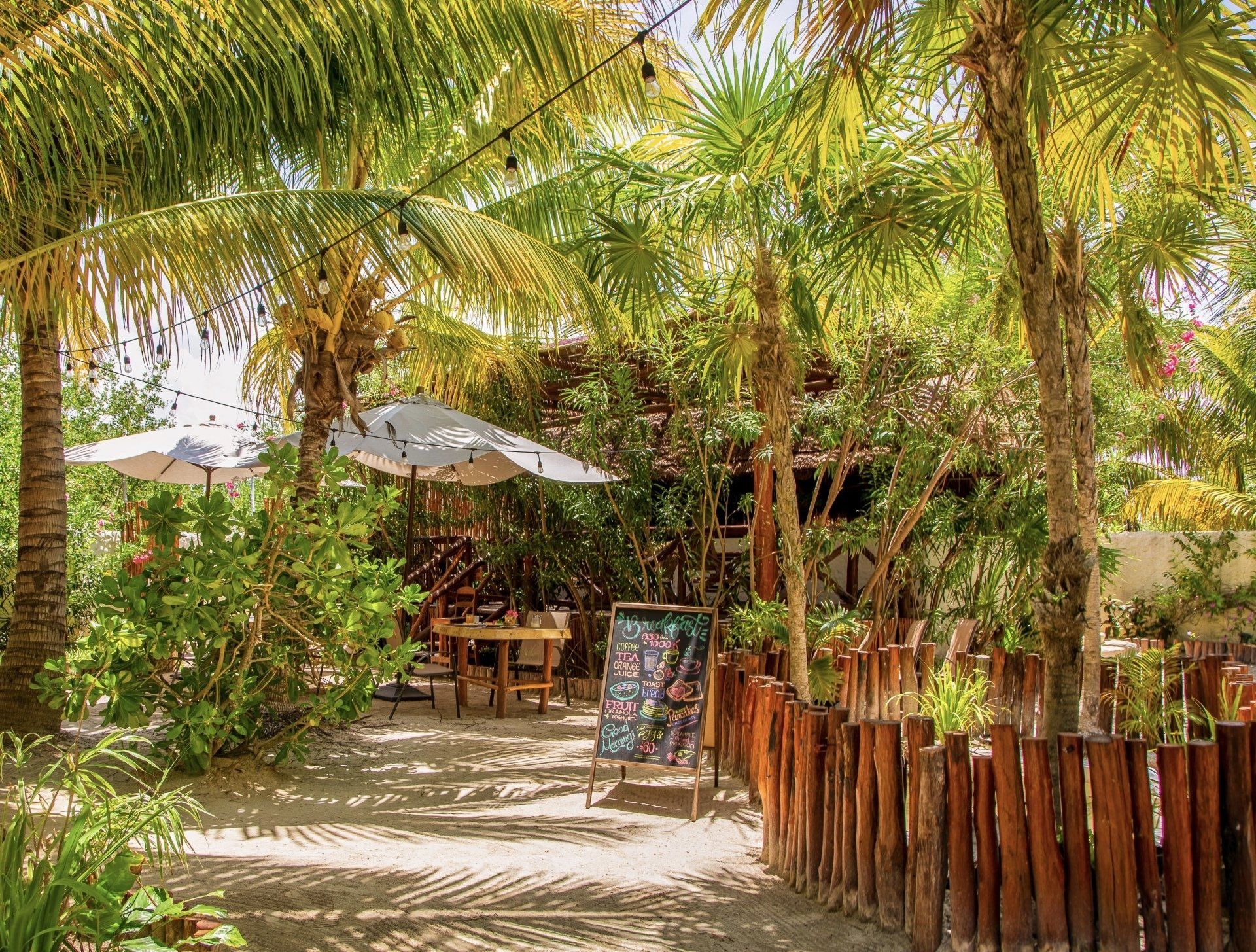A wooden fence surrounds a restaurant surrounded by palm trees.