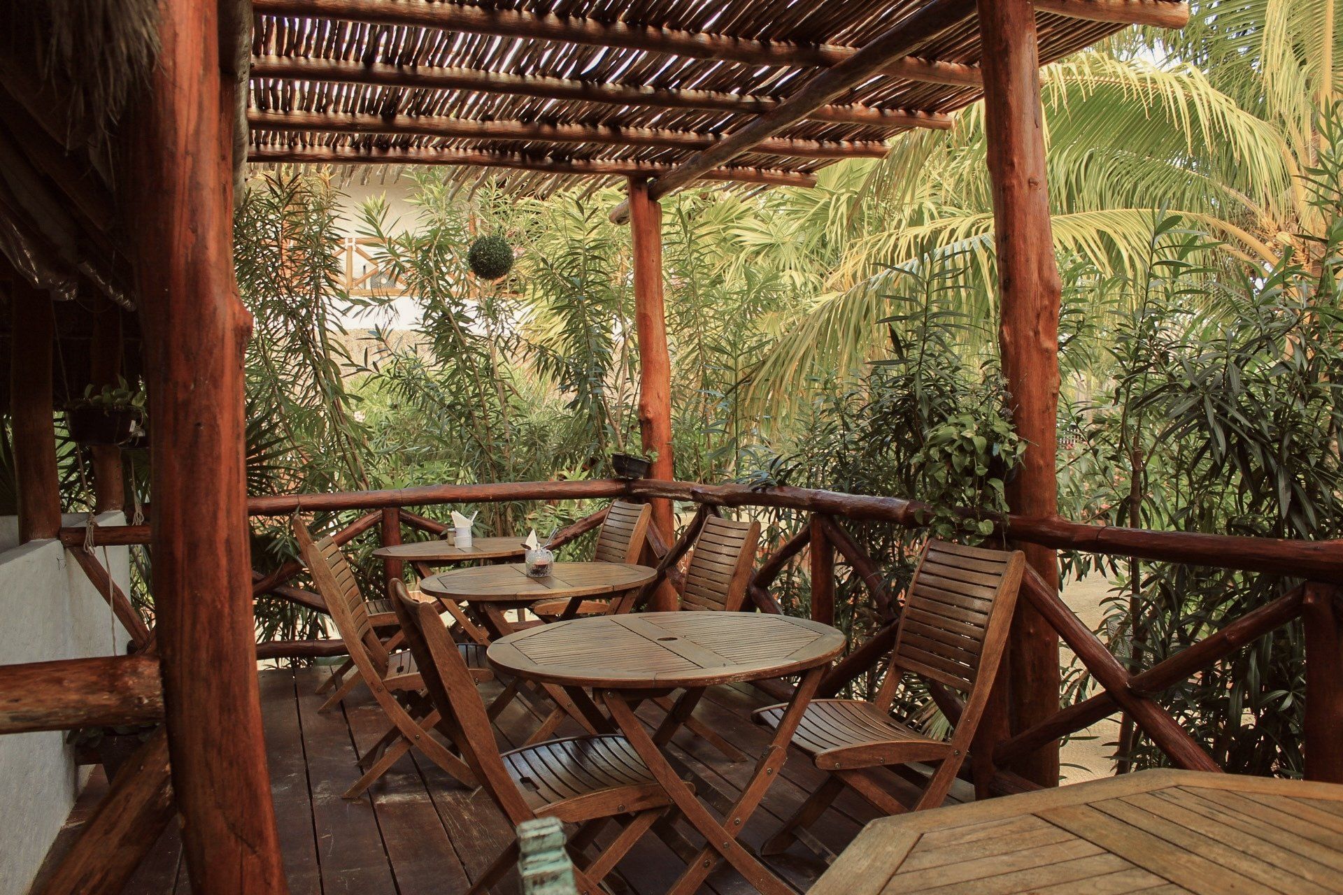 A wooden deck with tables and chairs under a thatched roof