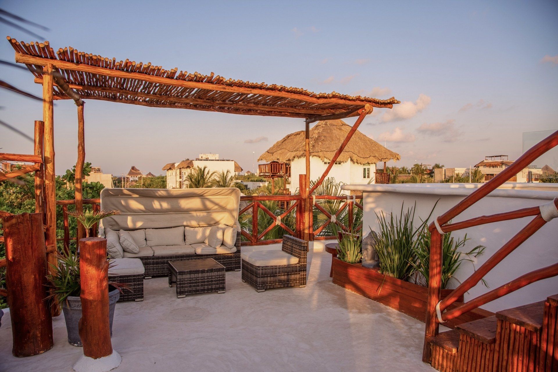 A rooftop terrace with a couch , table and chairs under a thatched roof.