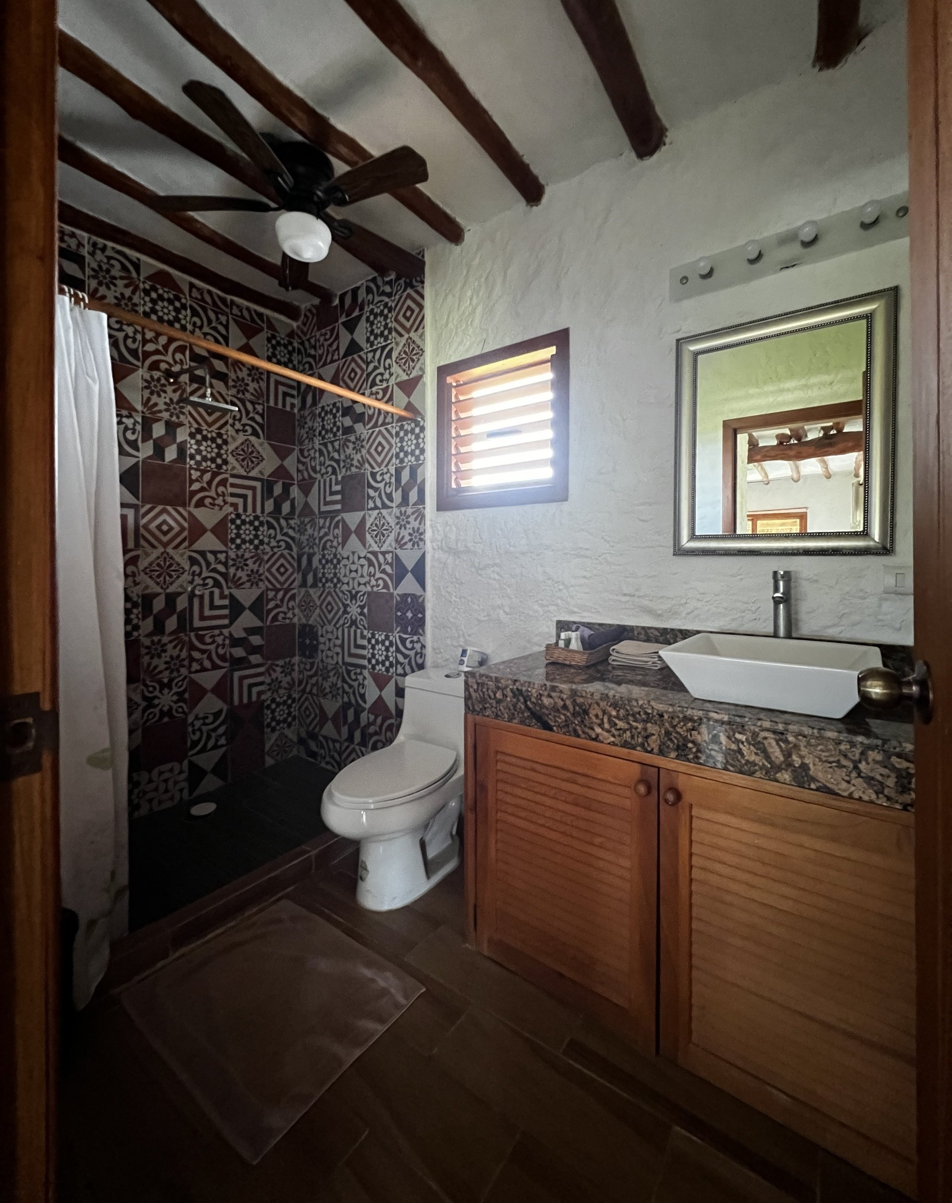Un baño con inodoro, lavabo, espejo y ventilador de techo.