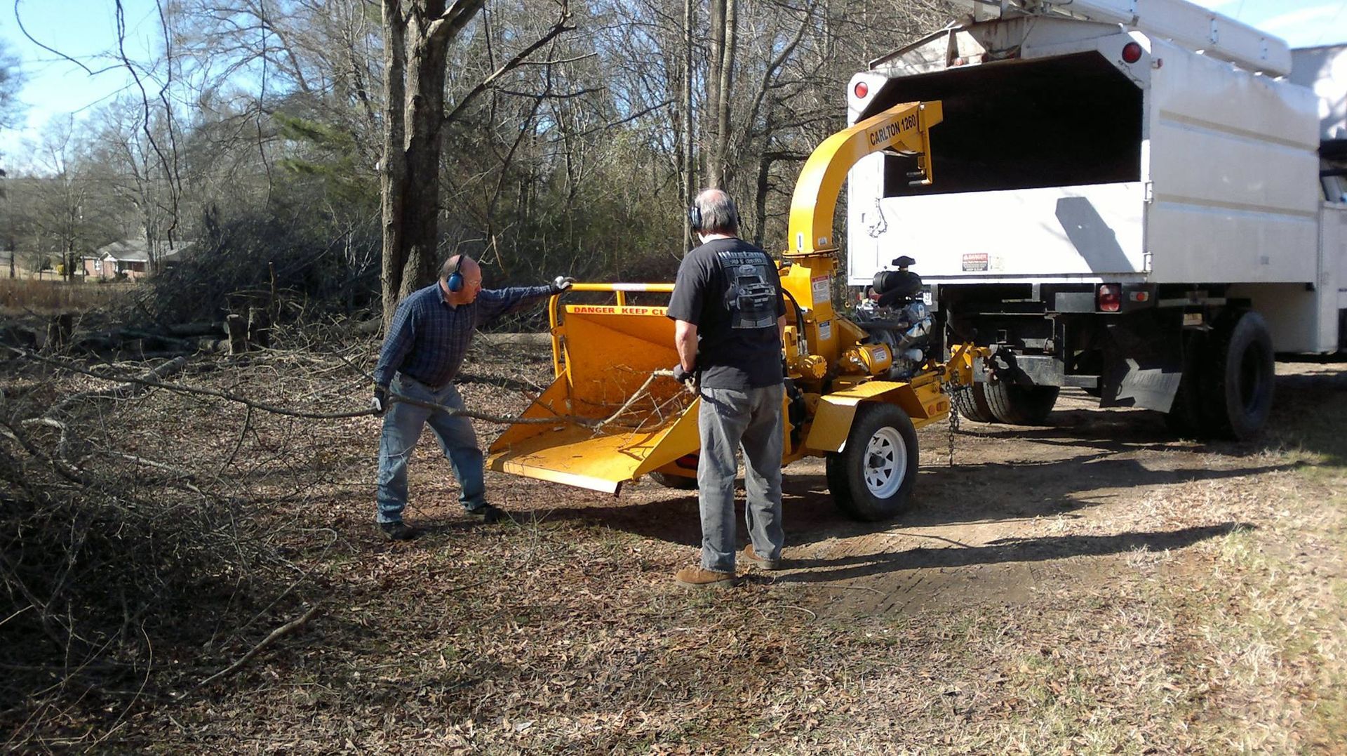A white truck with a crane attached to it is parked next to a tree
