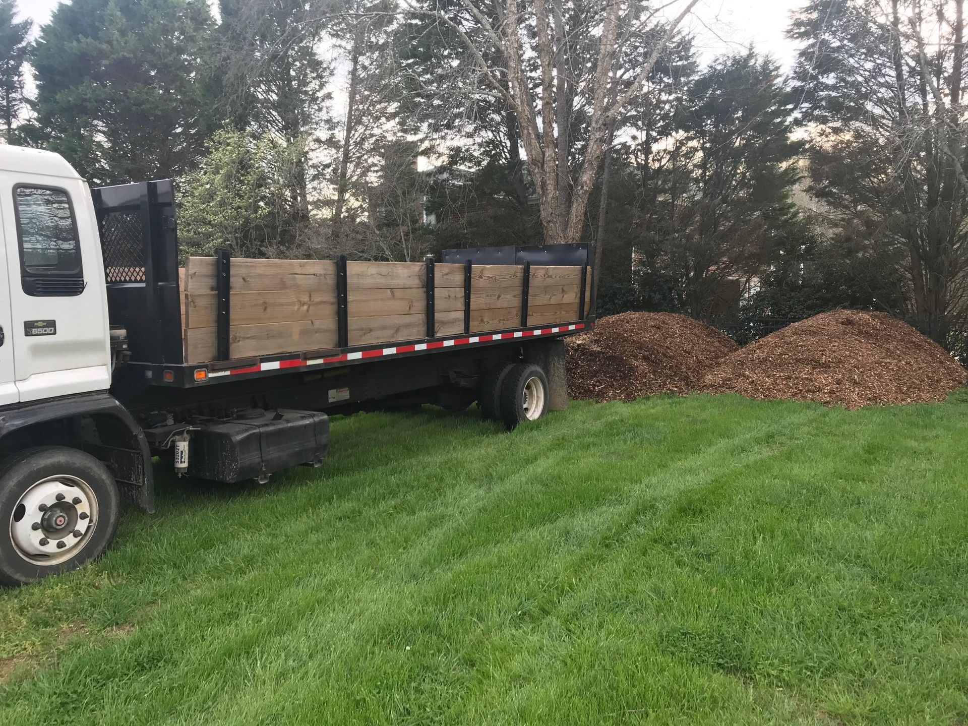 A dump truck is parked in a grassy field next to a pile of mulch.
