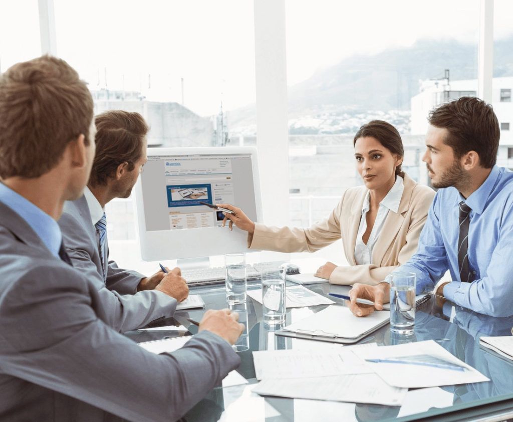 Reunión de negocios en una oficina luminosa, el equipo discute una presentación en un monitor con documentos sobre la mesa.