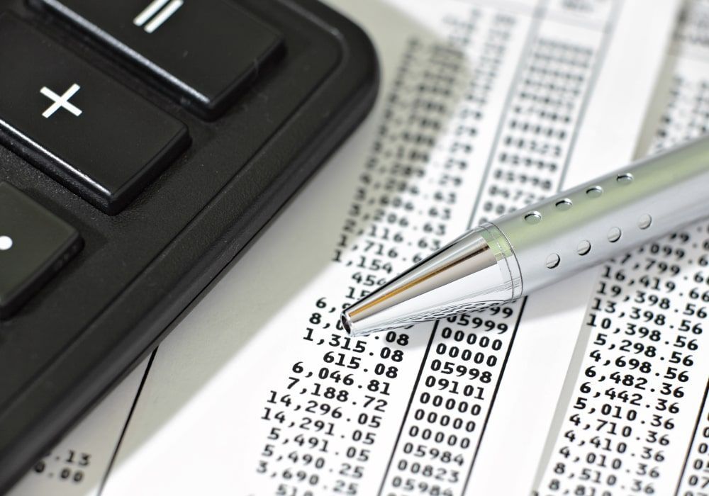 Calculadora y bolígrafo sobre una hoja de cálculo financiera con números resaltados.