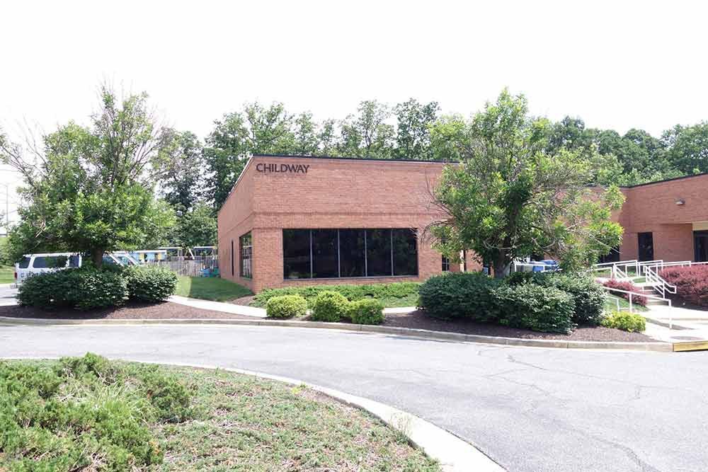 Brick office building with large windows, surrounded by trees, shrubs, and a curved driveway