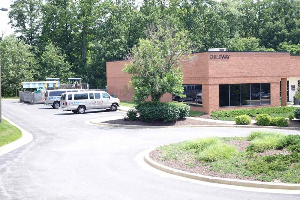 Brick office building with parked vans and trees in a curved driveway