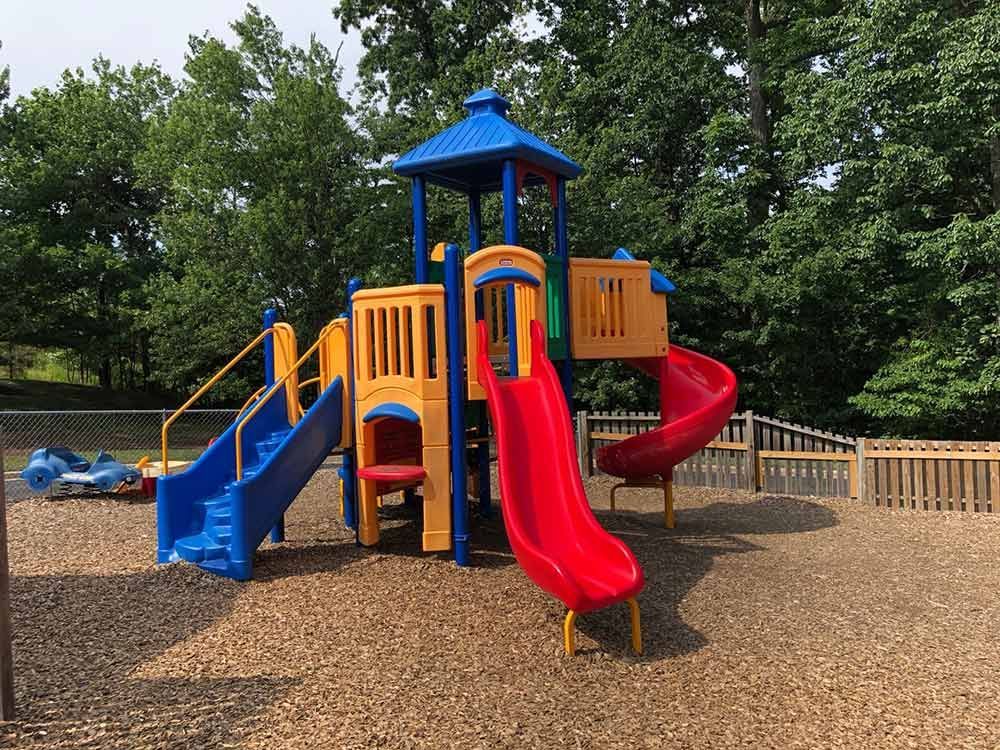 Colorful playground with blue and red slides, climbing structure, and wood-chip ground in a park.