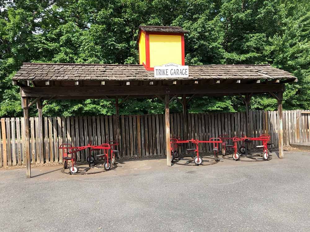 Red tricycle parking area beneath a wooden shelter labeled “THE DANCE” surrounded by trees