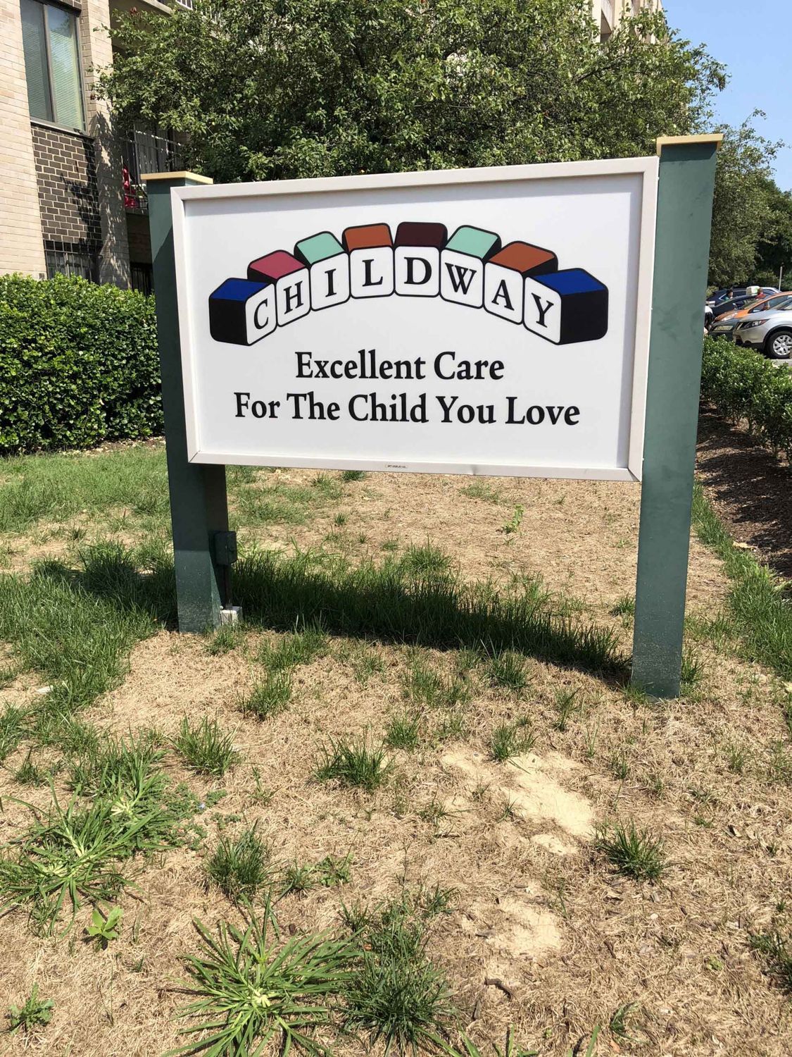 Childway childcare sign in a grassy outdoor area, white sign with colorful letters and slogan.