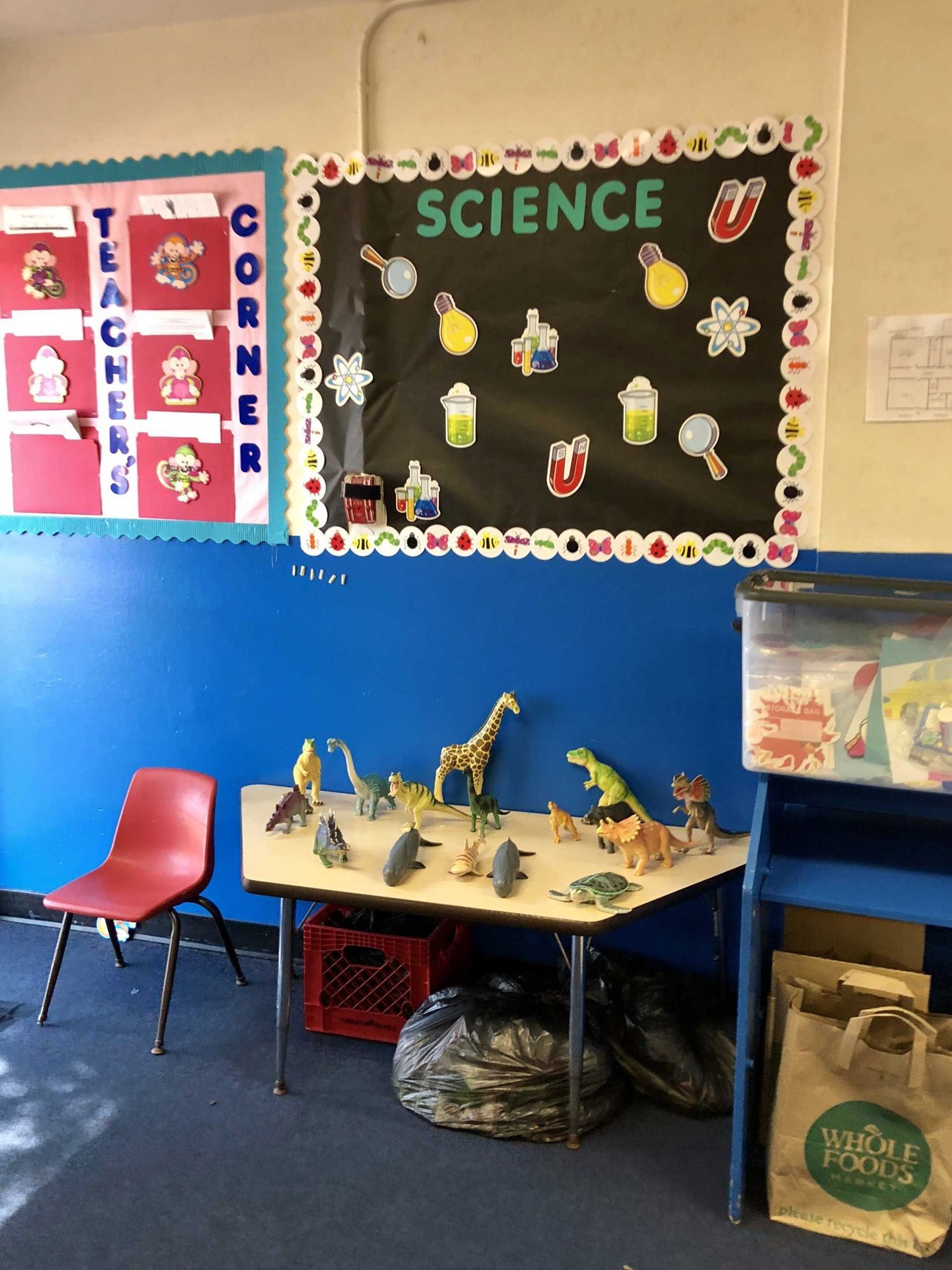 Classroom science display with child-made models on a table, red chair, and colorful bulletin boards