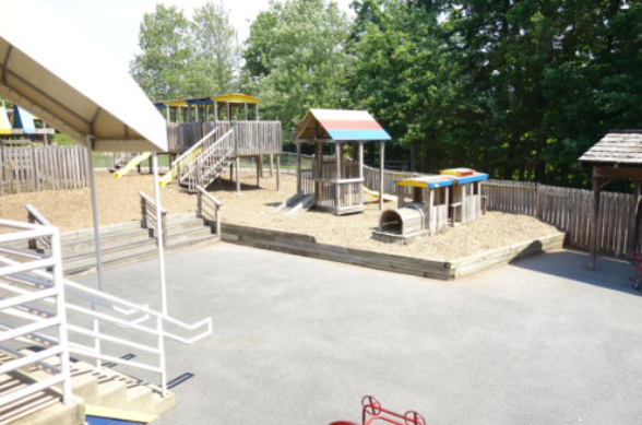 Empty school playground with slide, playhouse, and climbing structure on a paved surface