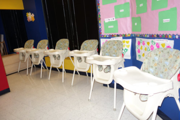 Row of white high chairs in a classroom-like room with colorful bulletin boards on the wall