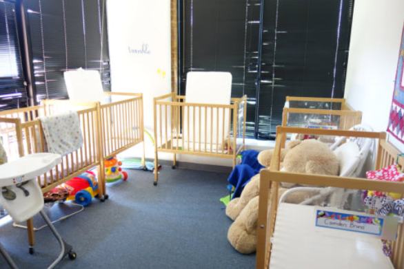 Children’s playroom with wooden cribs, toys, and a large teddy bear near a bright window