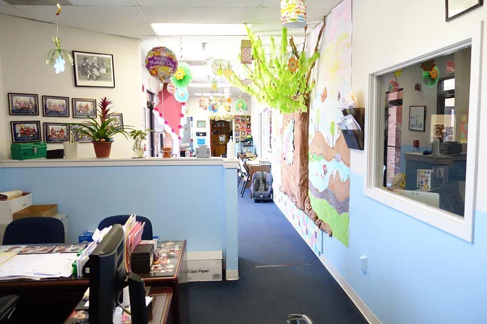 Bright office hallway with a front desk, framed photos, colorful balloons, and a wall map display.
