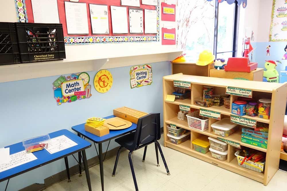 Colorful preschool classroom with tables, chairs, shelves of books, and wall charts