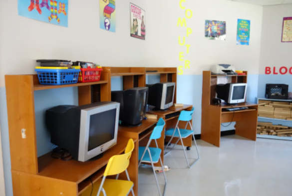 Computer lab with CRT monitors, colorful chairs, and wooden desks in a bright classroom