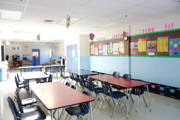 Empty classroom with tables, black chairs, and colorful bulletin boards along the wall.