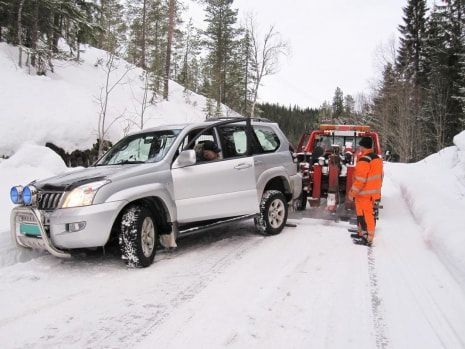 A silver suv is being towed by a tow truck in the snow