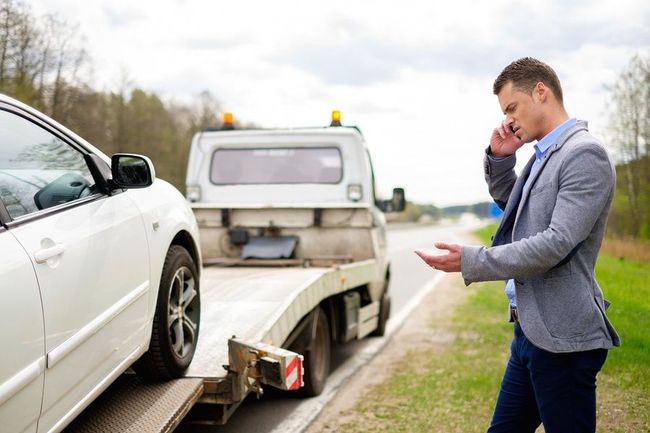 A man is talking on a cell phone next to a tow truck.