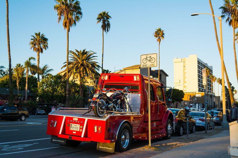 A red tow truck with a motorcycle on the back is parked on the side of the road.