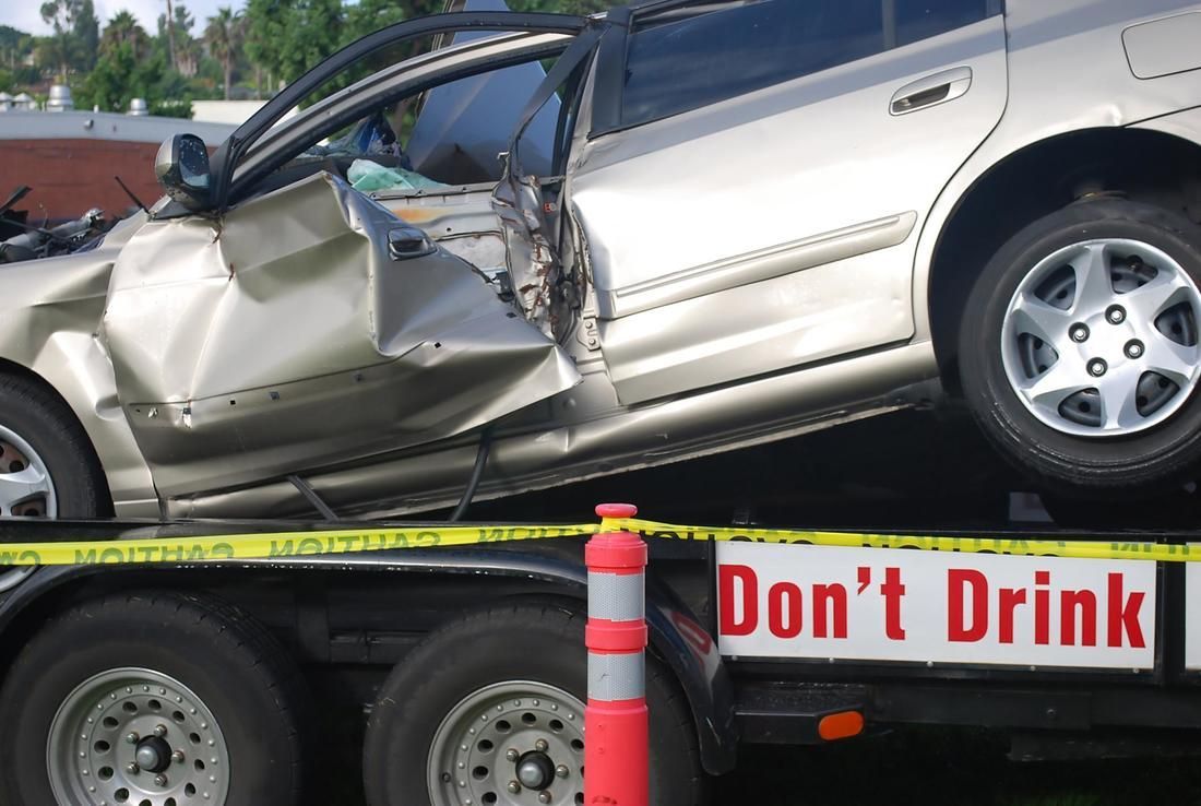 A damaged car is on a trailer with a sign that says do n't drink