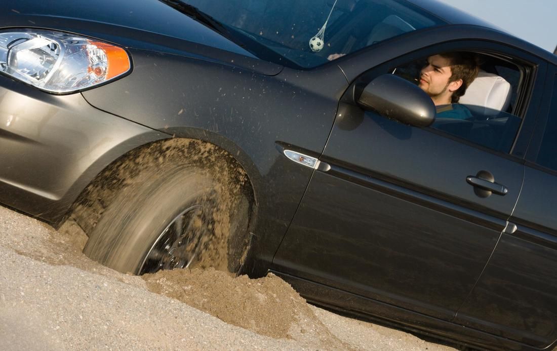 A man is driving a car that is stuck in the mud
