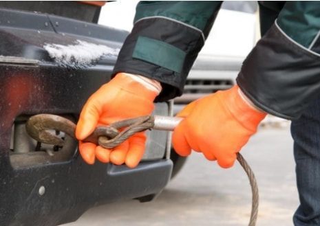 A person wearing orange gloves is towing a car