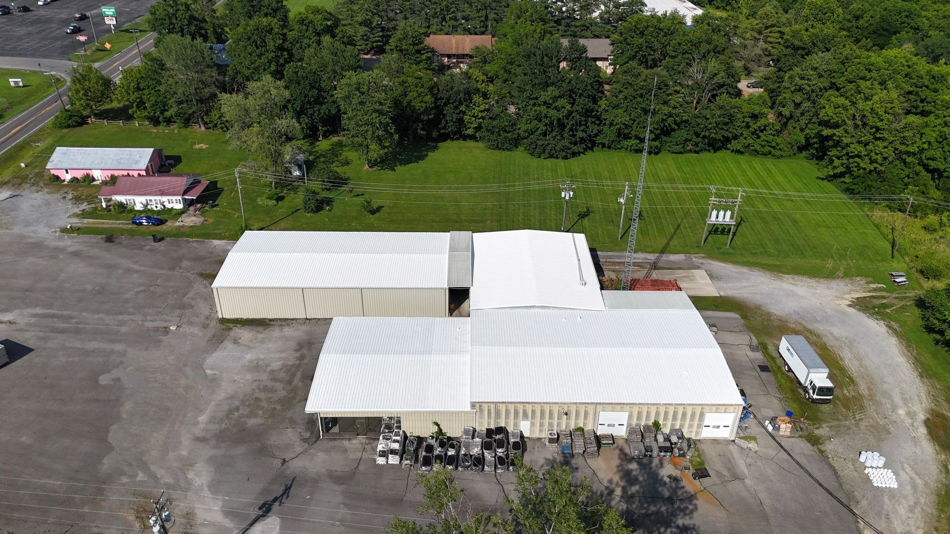 Aerial view of tan industrial buildings with white roofs, surrounded by trees and a parking lot.