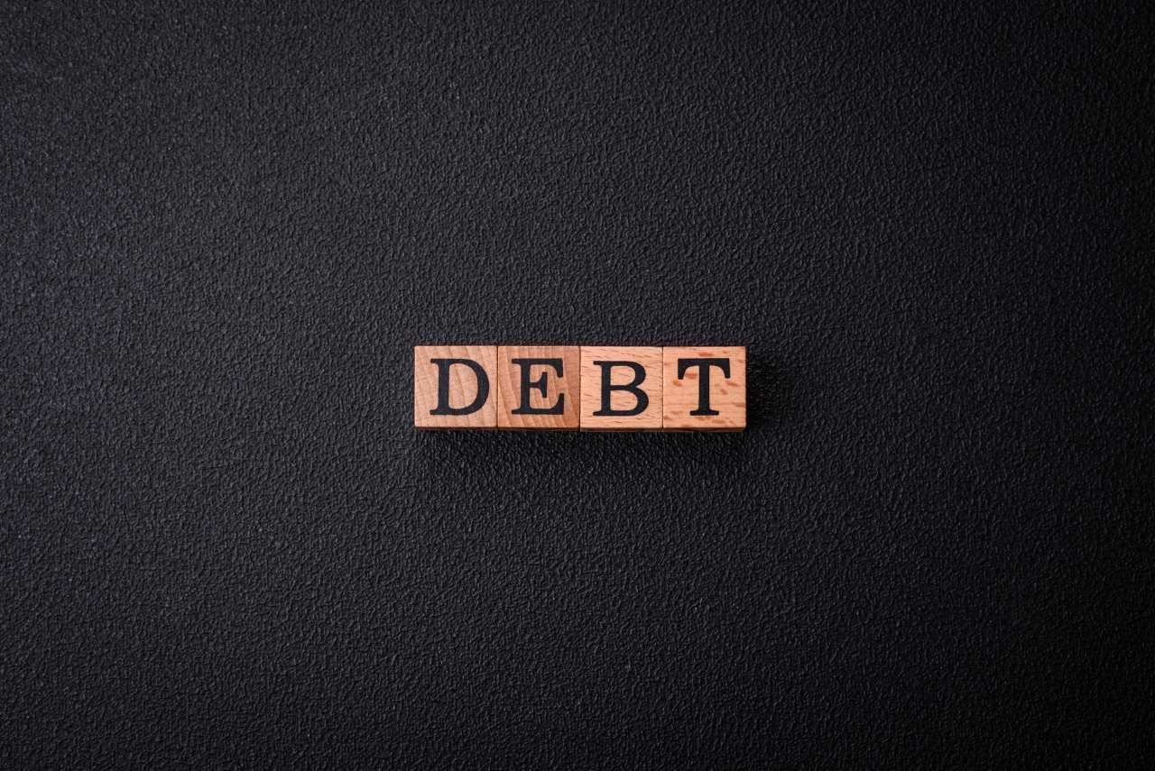 word debt spelled on small wooden blocks on a black background