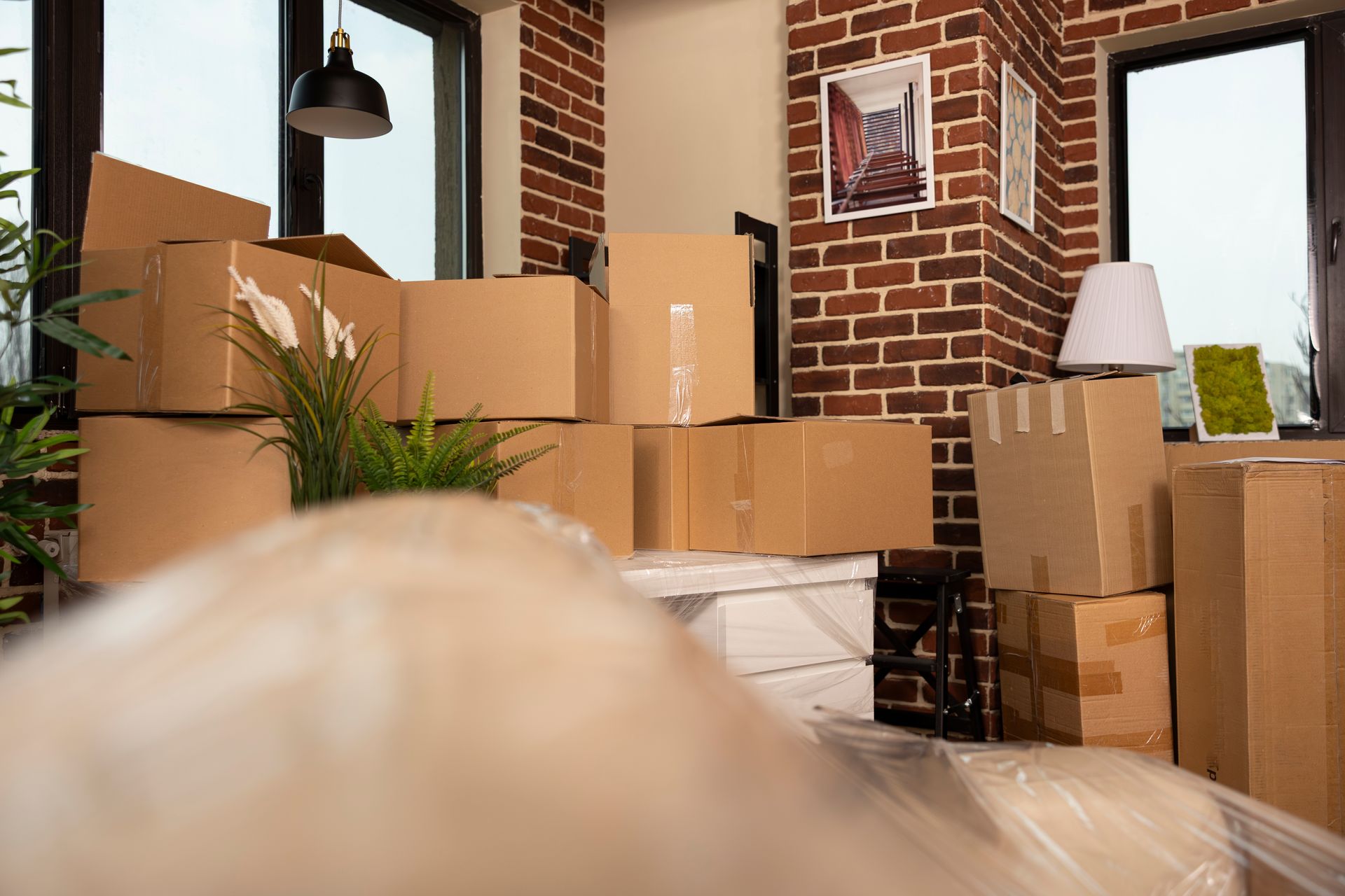 Packed moving boxes in a bright room with brick walls and a floor lamp