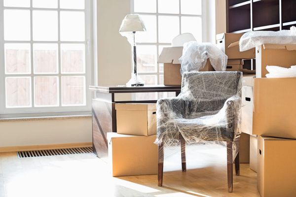 Wrapped chair and boxes in a bright room with a large window and floor lamp