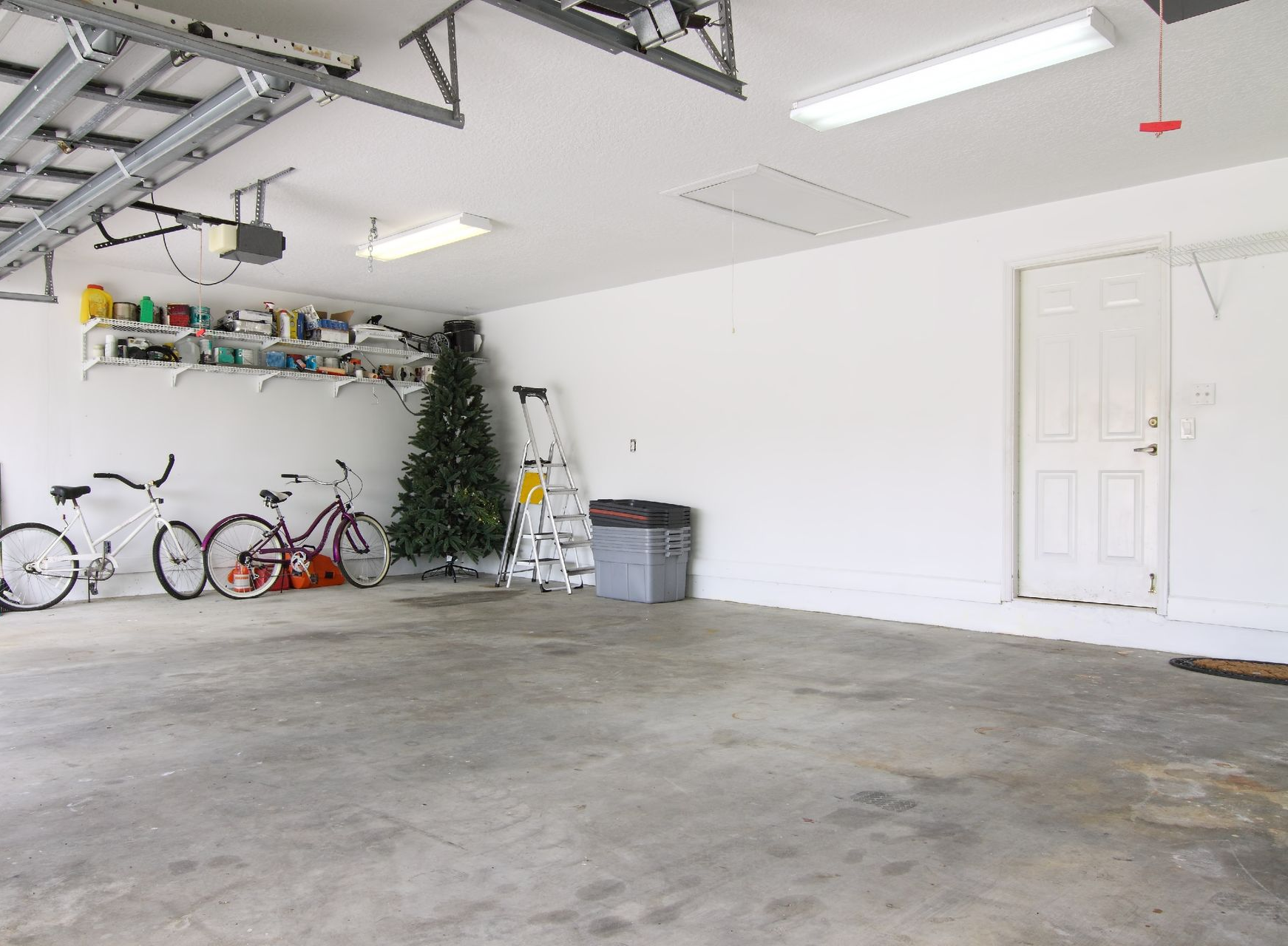 Spacious garage with bicycles, shelves, a Christmas tree, and a white door on the right.