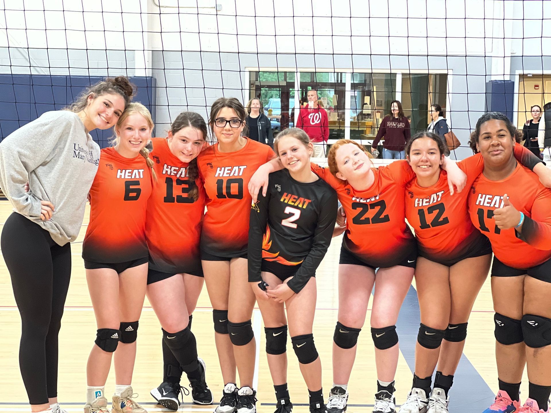 A group of girls are posing for a picture on a volleyball court.