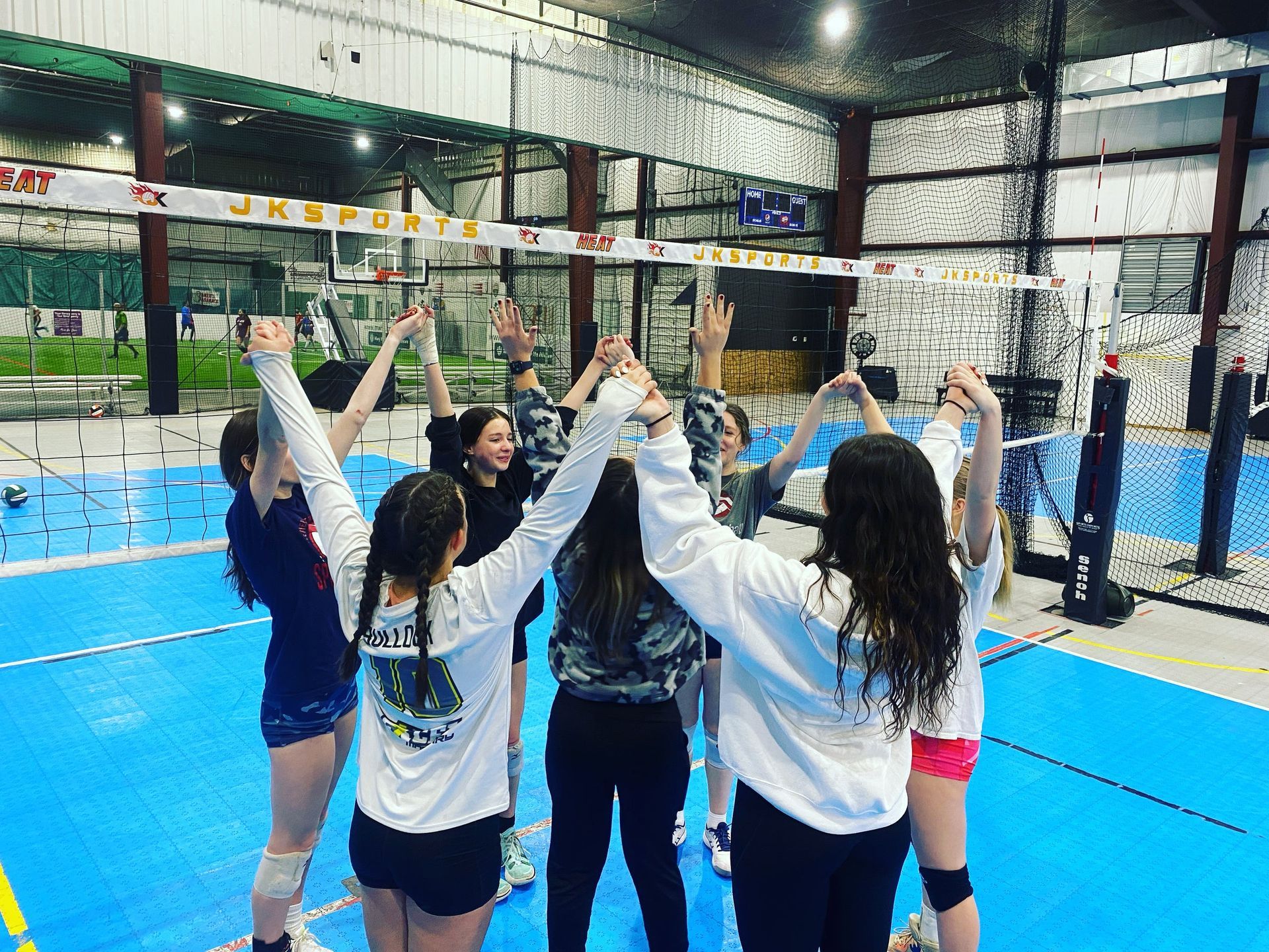A group of volleyball players are standing in a huddle with their arms in the air.