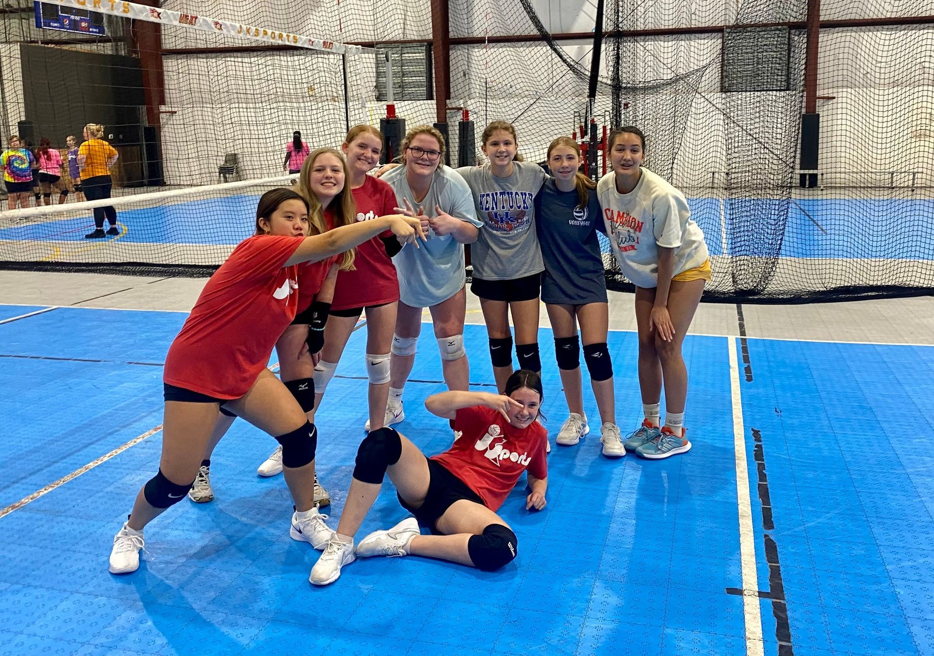 A group of young girls are posing for a picture on a volleyball court.