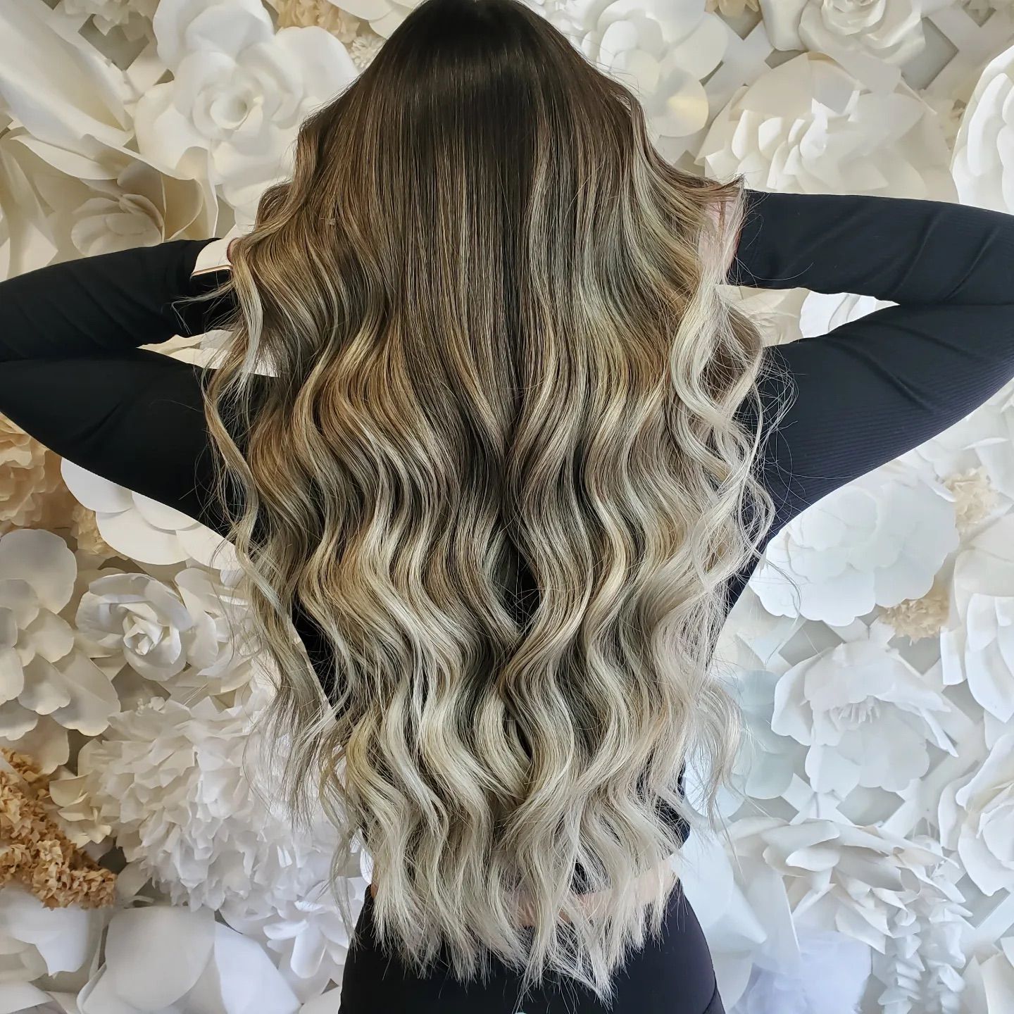Back of wavy blonde hair that is darker at crown and lightens up as it reaches below her waist showing balayage highlights.