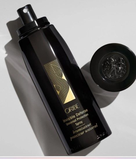 Tall black bottle with gold zigzag logo and Oribe Invisible Defense Universal Protection Spray printed on it.