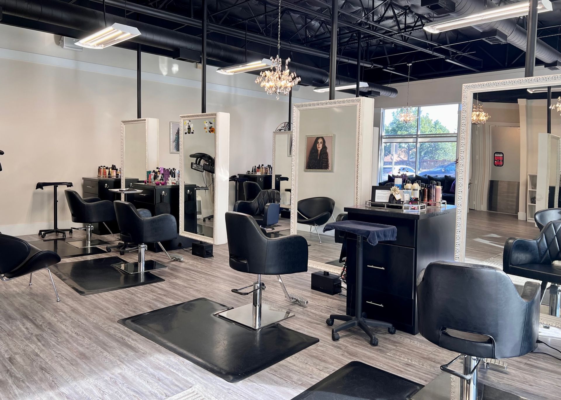 Seeing more of salon with 3 large framed mirrors in front of 3 black styling chairs.