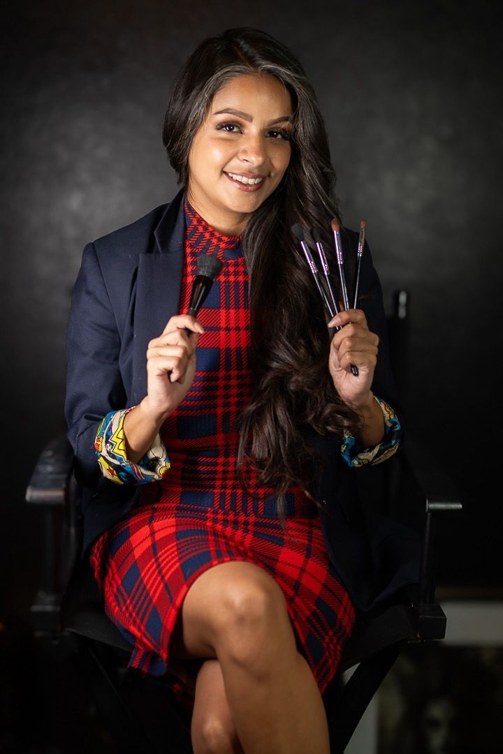 Smiling young make-up artist  with medium skin tone holding up cosmetic brushes.