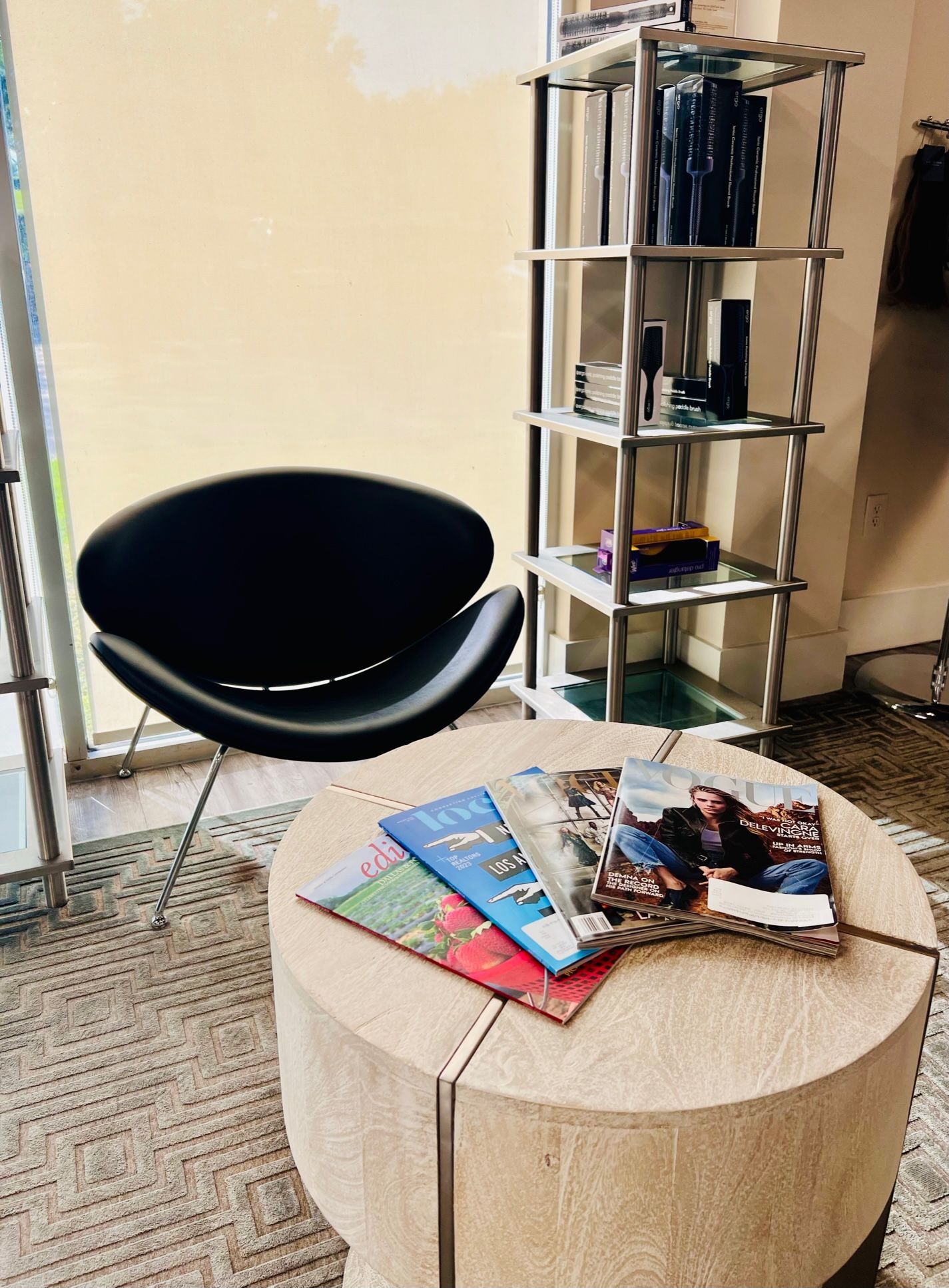Close-up of a black chair in salon waiting area with small round table with magazines.